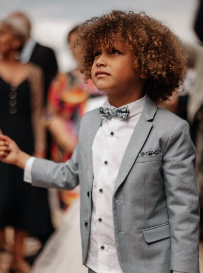 Diverse Kid with curly hair wearing a tie and a suit holding his father’s finger